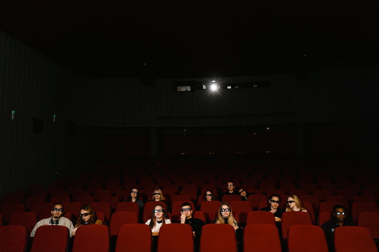 A group of people in a cinema watching a 3D movie wearing glasses, sitting in a dark theater.